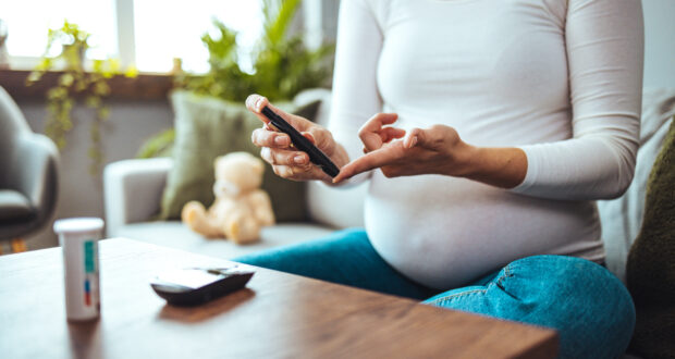 Happy Pregnant woman with glucometer checking blood sugar level at home. Woman testing for high blood sugar. Pregnant Woman holding device for measuring blood sugar