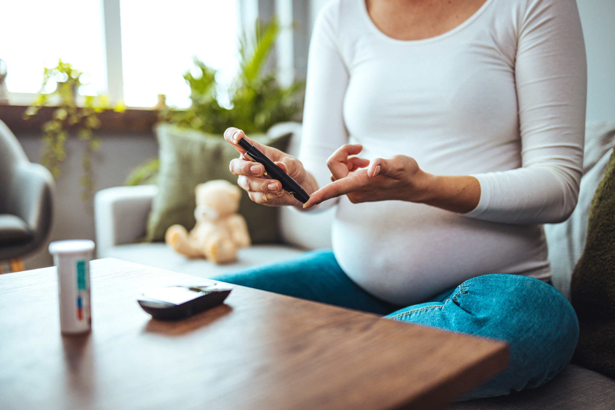 Happy Pregnant woman with glucometer checking blood sugar level at home. Woman testing for high blood sugar. Pregnant Woman holding device for measuring blood sugar