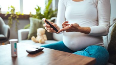 Happy Pregnant woman with glucometer checking blood sugar level at home. Woman testing for high blood sugar. Pregnant Woman holding device for measuring blood sugar