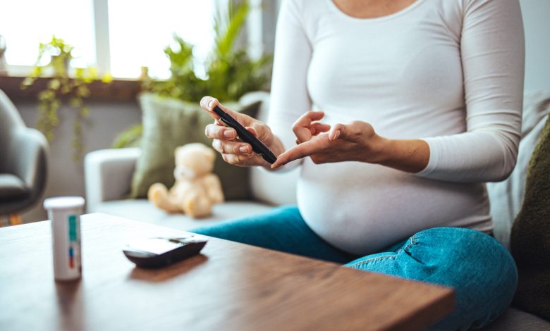 Happy Pregnant woman with glucometer checking blood sugar level at home. Woman testing for high blood sugar. Pregnant Woman holding device for measuring blood sugar