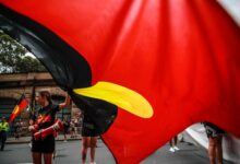 SYDNEY, AUSTRALIA - JANUARY 26: Demonstrators hold up an Aboriginal flag during an Invasion Day protest on January 26, 2024 in Sydney, Australia. Australia Day, formerly known as Foundation Day, is the official national day of Australia and is celebrated annually on January 26 to commemorate the arrival of the First Fleet to Sydney in 1788. Many indigenous Australians refer to the day as 'Invasion Day' and there is a growing movement to change the date to one which can be celebrated by all Australians. In 2024, supermarket Chains Woolworths and Aldi announced that they would stop stocking themed merchandise for the day, drawing a political backlash from opposition leader Peter Dutton. (