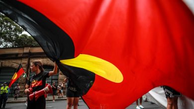 SYDNEY, AUSTRALIA - JANUARY 26: Demonstrators hold up an Aboriginal flag during an Invasion Day protest on January 26, 2024 in Sydney, Australia. Australia Day, formerly known as Foundation Day, is the official national day of Australia and is celebrated annually on January 26 to commemorate the arrival of the First Fleet to Sydney in 1788. Many indigenous Australians refer to the day as 'Invasion Day' and there is a growing movement to change the date to one which can be celebrated by all Australians. In 2024, supermarket Chains Woolworths and Aldi announced that they would stop stocking themed merchandise for the day, drawing a political backlash from opposition leader Peter Dutton. (