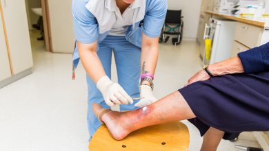 Cute Nurse with tatoo on her forearm is changing bandage to a patient with venous insufficiency ulceration...wheel chair on back