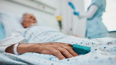 Close up of elderly patient lying down in hospital bed with pulse oximeter on his finger.