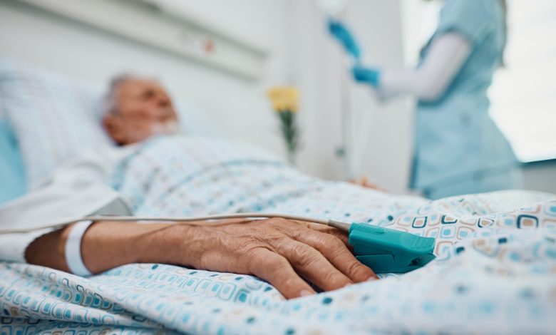 Close up of elderly patient lying down in hospital bed with pulse oximeter on his finger.