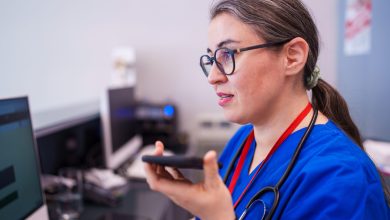 A healthcare worker sits at a desk, focused on using their phone. The scene captures the daily administrative tasks and communication that healthcare professionals manage in a medical setting.