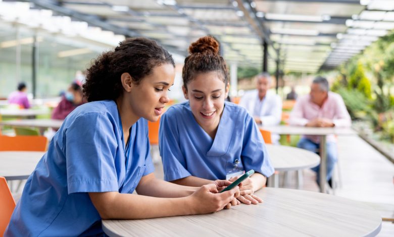 Nurses taking a break from work at the hospital and looking at social media on a cell phone at the cafeteria