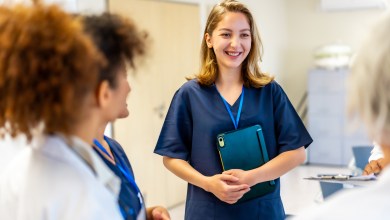 Young nurse smiling and engaging with colleagues while holding a tablet in a bright hospital hallway, fostering teamwork and communication