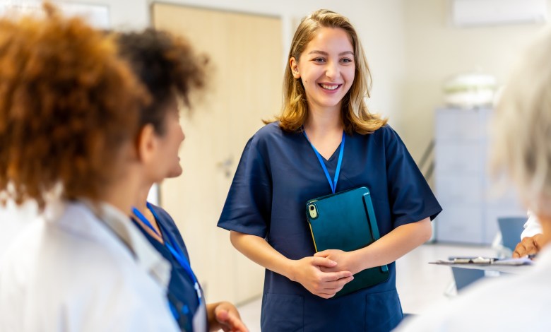 Young nurse smiling and engaging with colleagues while holding a tablet in a bright hospital hallway, fostering teamwork and communication