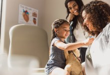 Joyful child plays doctor with stethoscope on teddy bear during a family medical visit.