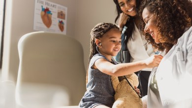 Joyful child plays doctor with stethoscope on teddy bear during a family medical visit.