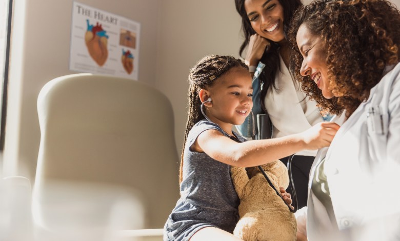 Joyful child plays doctor with stethoscope on teddy bear during a family medical visit.