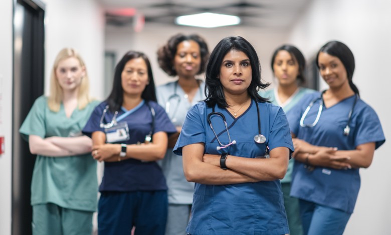 Portrait of a team of female nurses and doctors. The multi-ethnic medical professionals are standing in a corridor of a hospital. The confident group is looking directly at the camera. They have serious expressions on their faces and their arms are crossed. A doctor of Indian descent is standing at the front of the group.