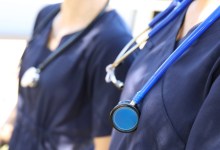 Two female medical practicioners in blue uniform with stethoscopes around their necks. Nursing or doctors in hospital gowns or clothes. Health, hospitals and medical themed image.