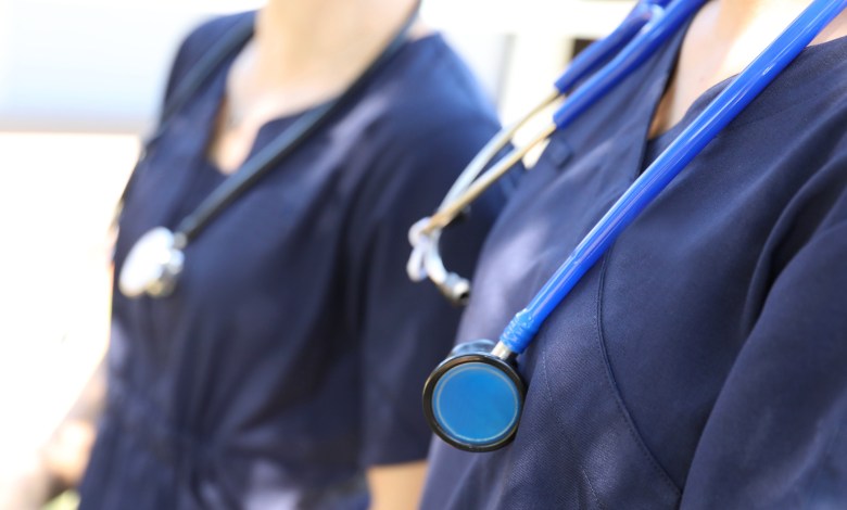 Two female medical practicioners in blue uniform with stethoscopes around their necks. Nursing or doctors in hospital gowns or clothes. Health, hospitals and medical themed image.