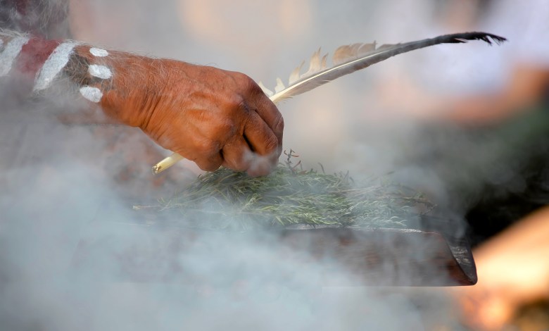 Human hand hold wooden dish and feather at the smoke ritual rite at a indigenous community event in Australia