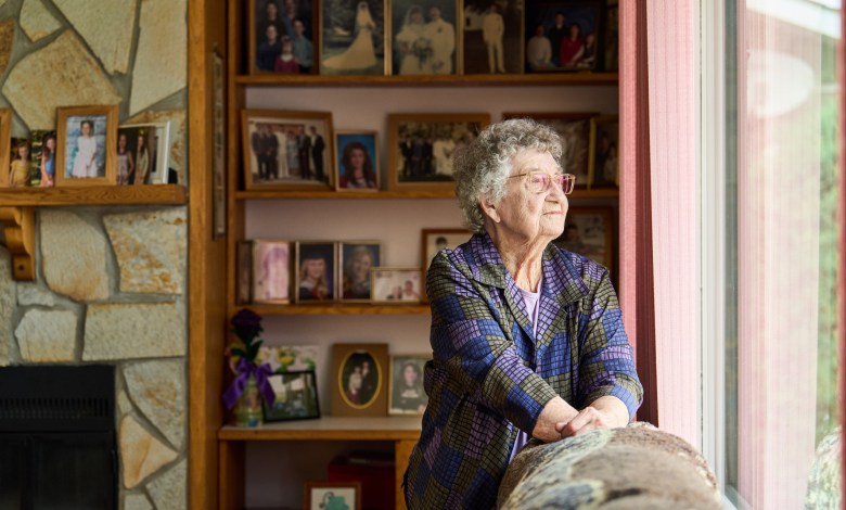 Senior woman wearing glasses lost in thought while looking out through a window in her living room at home