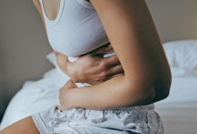 Menstruation, sick and stomach ache with black woman in bedroom for indigestion, cramps and illness. Frustrated, gas and stress with girl on bed for constipation, bloating and intestine problems