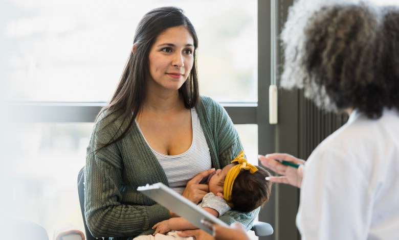 Young mother holding baby, discussing health with female doctor. Healthcare and medicine, pediatrics.