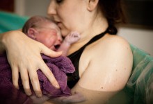 Color photo of a loving mother holding her newborn baby son in the water of a birthing tub immediately after a water birth at home.