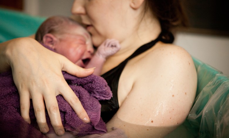 Color photo of a loving mother holding her newborn baby son in the water of a birthing tub immediately after a water birth at home.