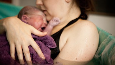 Color photo of a loving mother holding her newborn baby son in the water of a birthing tub immediately after a water birth at home.
